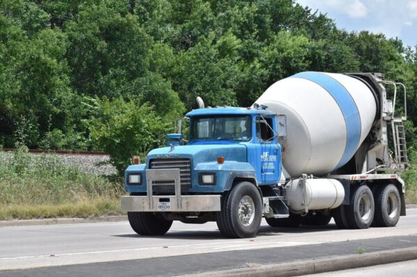 Blue and white redi mix concrete truck on roadway in front of trees and railroad track